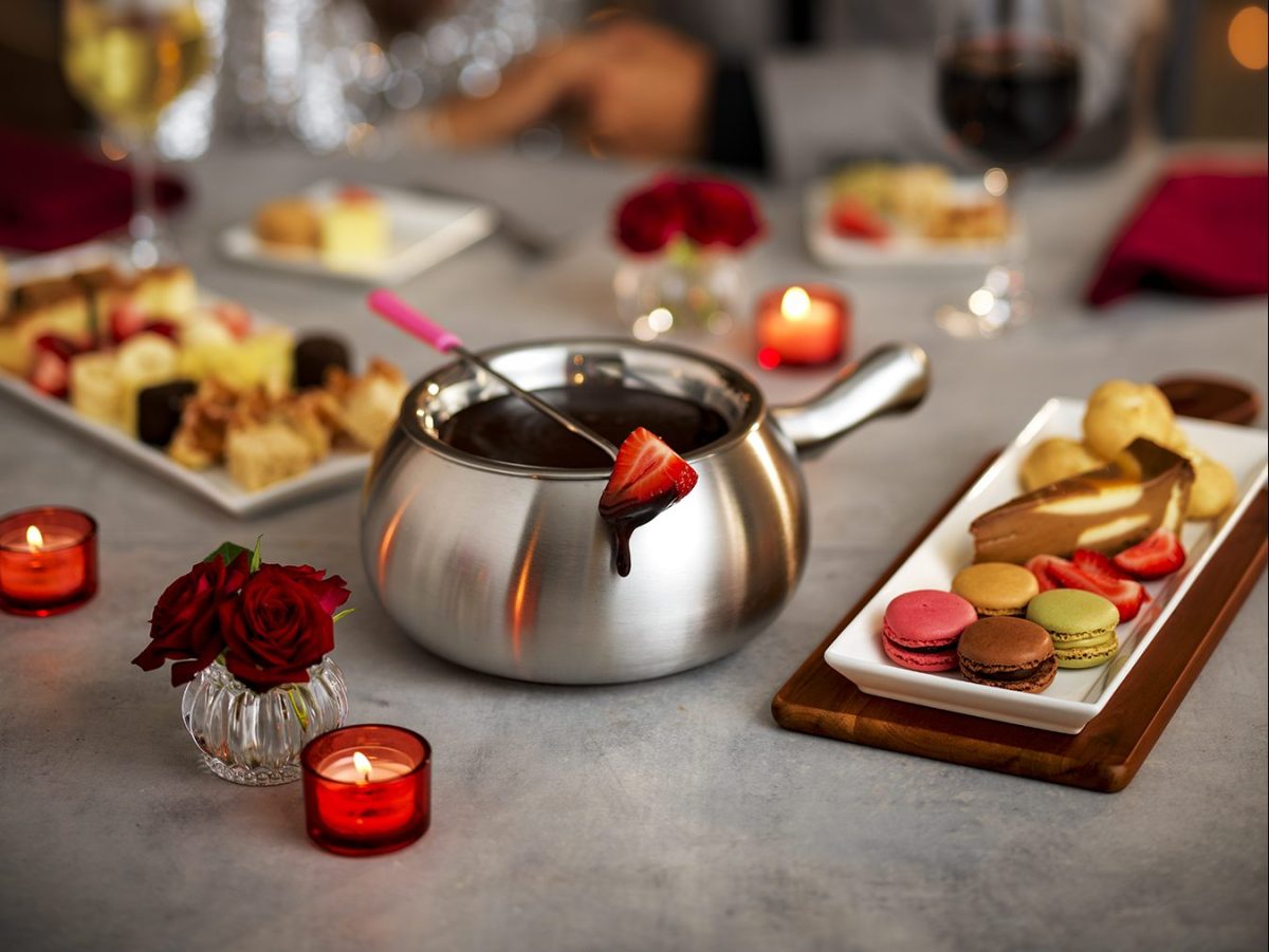 A large metal bowl filled with chocolate fondue with a skewer with a strawberry on it on top.