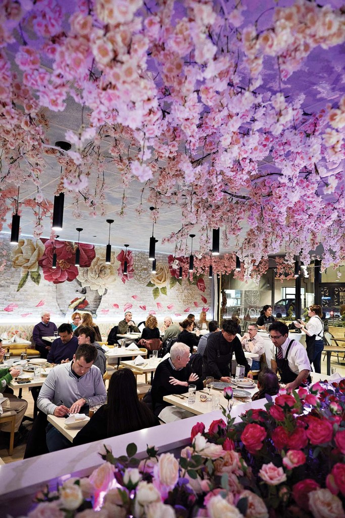 a restaurant with diners at small tables. the ceiling and walls feature many pink and white flowers