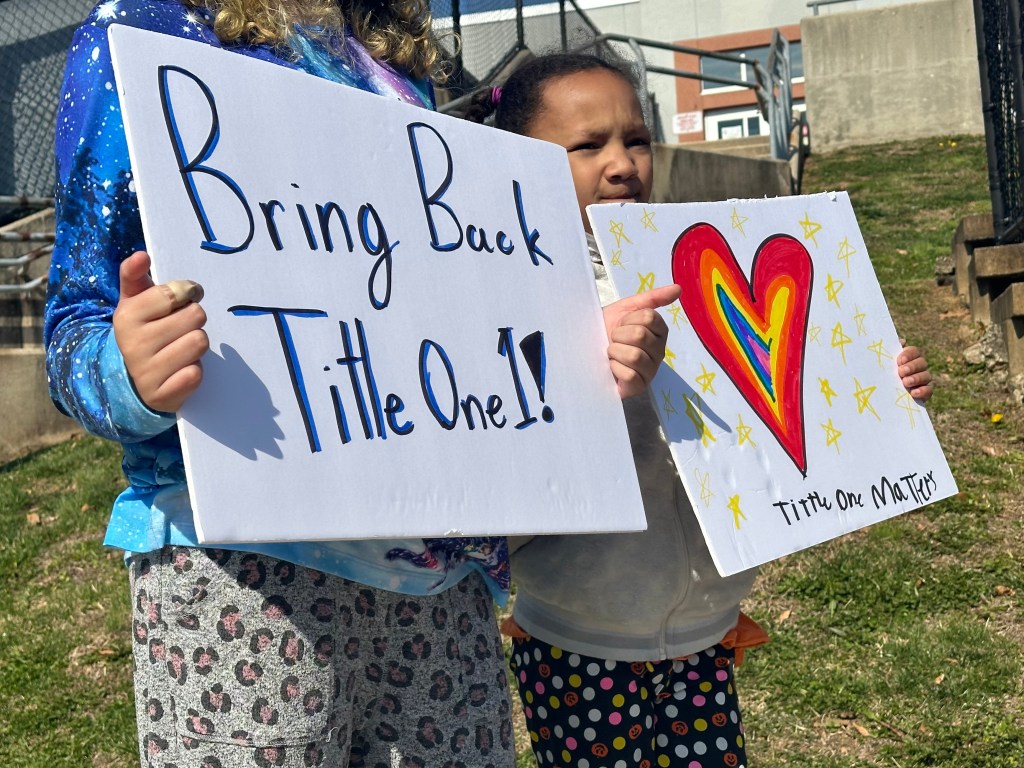 Two students hold handmade posted that read: "Bring back Title One!" and "Title One Matters."
